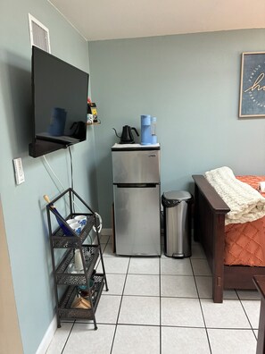 A compact kitchenette with a refrigerator, a coffee maker, and a small trash bin. - Newly renovated beach house in quiet neighborhood, close to everything! (New Smyrna Beach)