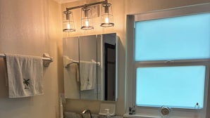 Une salle de bain avec un meuble-lavabo blanc, des toilettes, une fenêtre et un miroir.