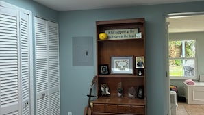 Une chambre avec un puits de lumière, un lit recouvert d’une couvre-lit à motifs, une commode en bois et une étagère contenant divers objets.