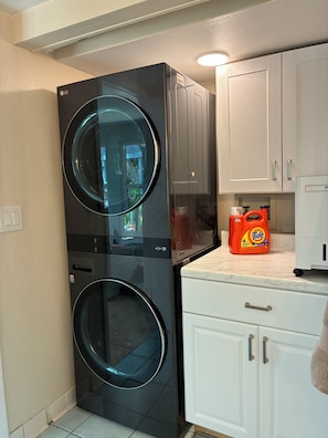 A compact kitchen with a black washing machine, white cabinets, and a bottle of Tide detergent on the counter. - Newly renovated beach house in quiet neighborhood, close to everything! (New Smyrna Beach)