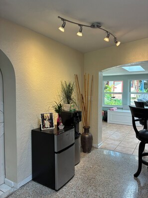 A kitchen with a refrigerator, a vase with plants, and a dining area with a chair. - Newly renovated beach house in quiet neighborhood, close to everything! (New Smyrna Beach)