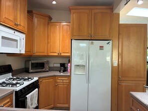 A kitchen with wooden cabinets, a white refrigerator, a microwave, a toaster oven, and a gas stove. - Newly renovated beach house in quiet neighborhood, close to everything! (New Smyrna Beach)