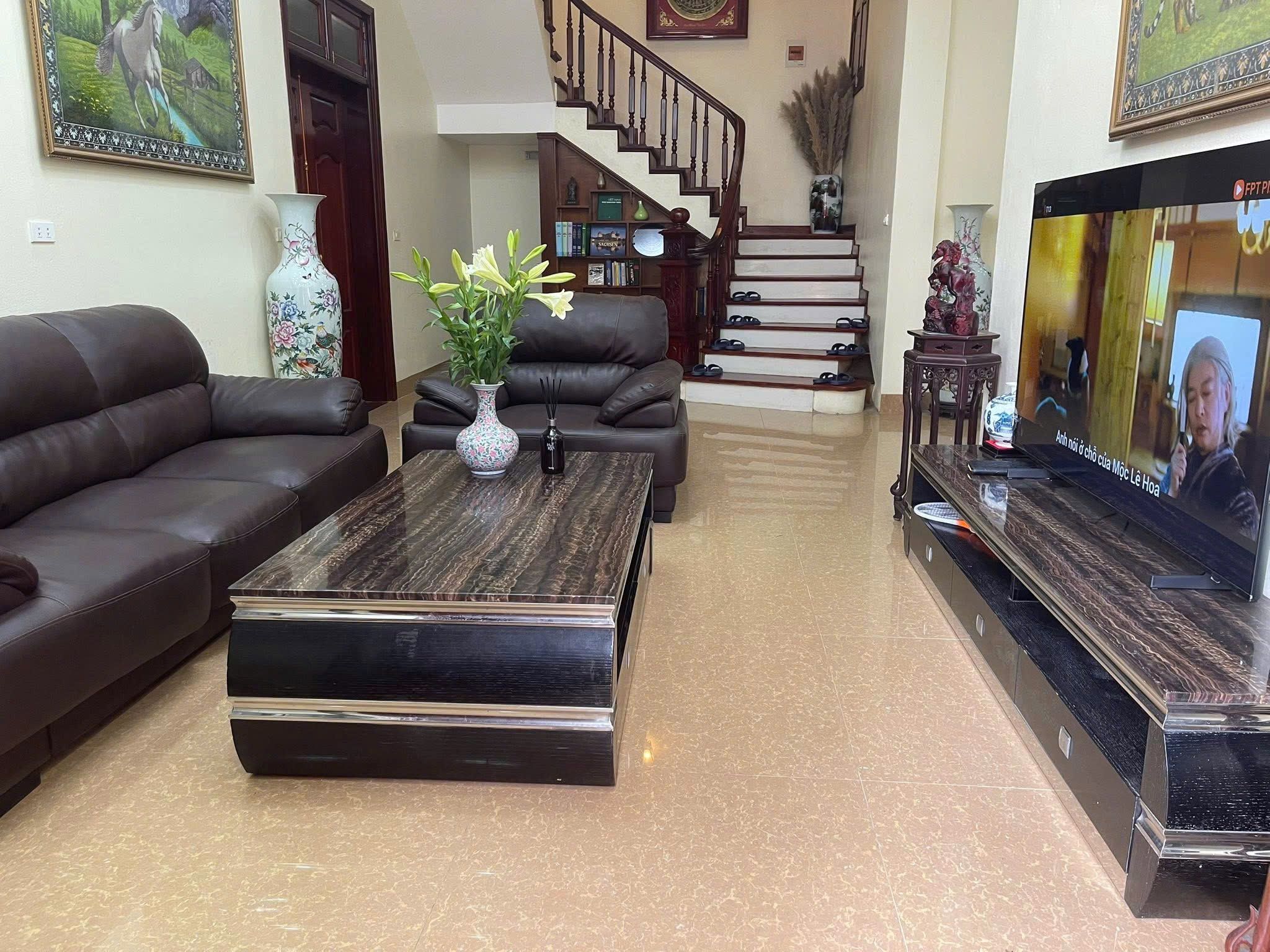 A living room with a sofa, a coffee table, and a TV. There is a staircase in the background.