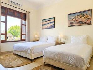 A hotel room with two beds, a large window, and artwork on the walls.