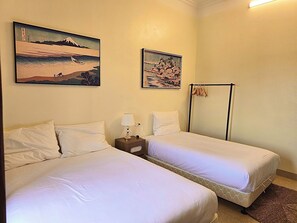 Quarto de hotel com duas camas, uma mesa de cabeceira com abajur e dois quadros pendurados na parede.