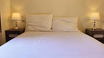 A bed with white linens, two bedside lamps, and a wall-mounted painting of a coastal scene.