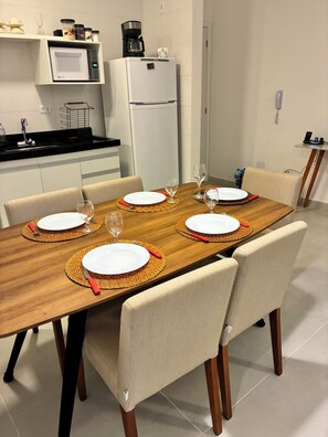 A dining area with a wooden table set for four, surrounded by chairs. - Brand new apartment. with complete leisure in the center (Ubatuba)