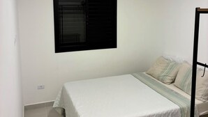 Ein Schlafzimmer mit einem Bett, einem Fenster mit heruntergelassenen Jalousien, einer Deckenleuchte und einer Wand-Klimaanlage.
