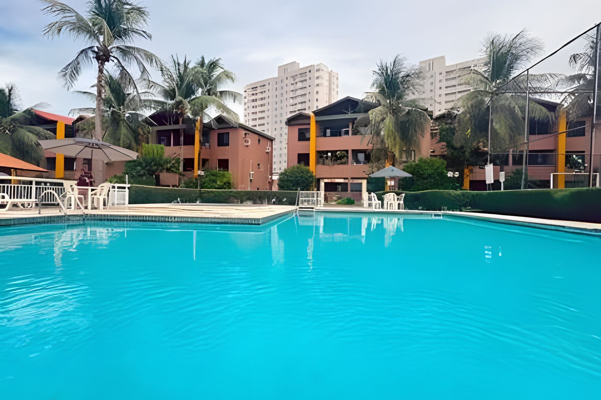 Une piscine à l’eau d’un bleu cristallin, entourée de palmiers et d’immeubles dotés de balcons.