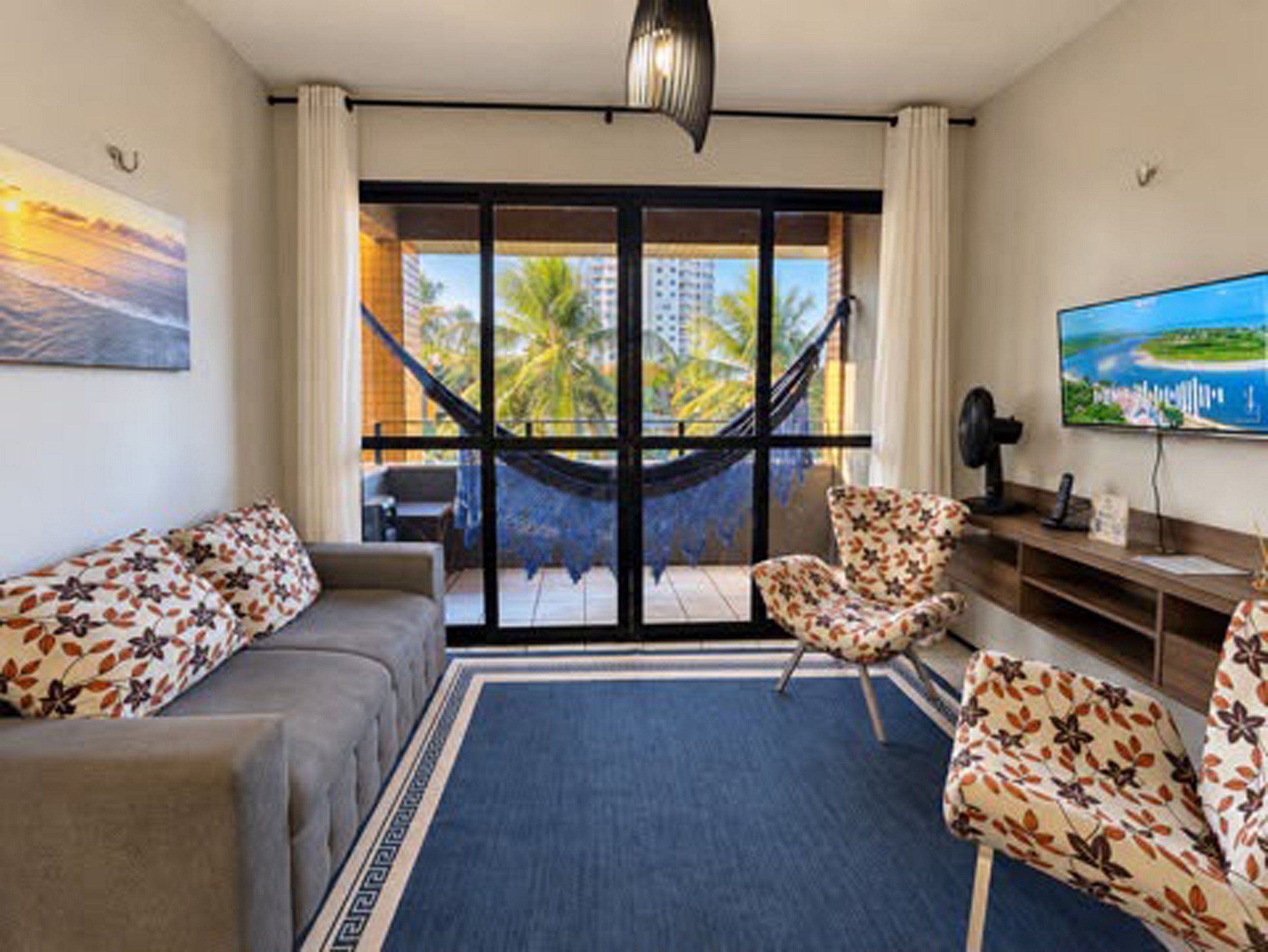 A hotel room with a sofa, armchair, TV, and a hammock.