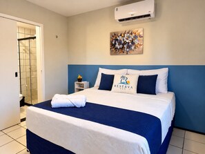 Ein Hotelzimmer mit Bett, Nachttisch, einem Gemälde und einer Klimaanlage.
