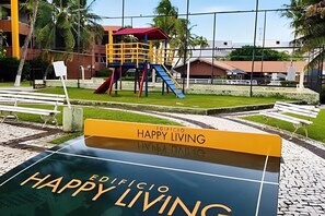 Ein Spielplatz mit Rutschen und einer Kletterkonstruktion, umgeben von Bänken und einem befestigten Bereich.