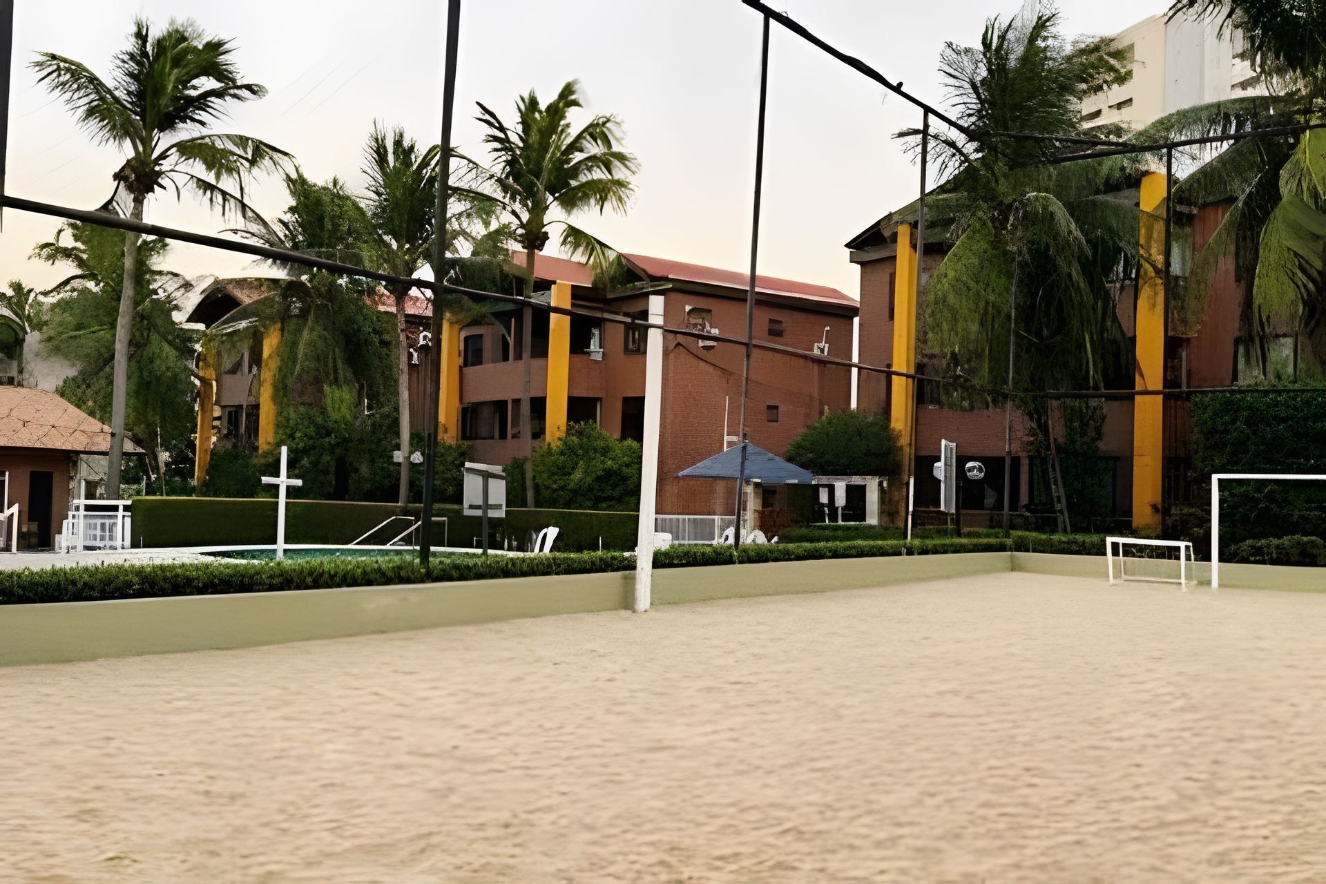 A tennis court with a net, surrounded by palm trees and buildings.