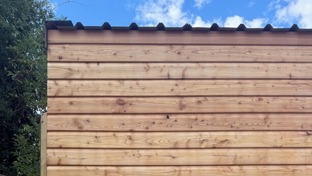 A wooden fence with a metal barrel and a potted plant with white flowers.