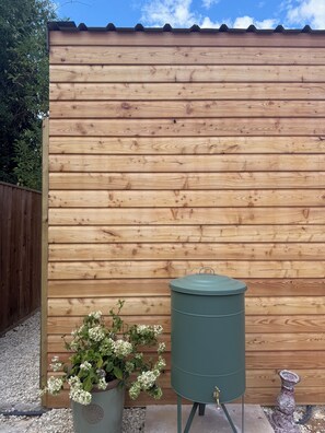 Una valla de madera con un barril metálico y una planta en maceta con flores blancas.