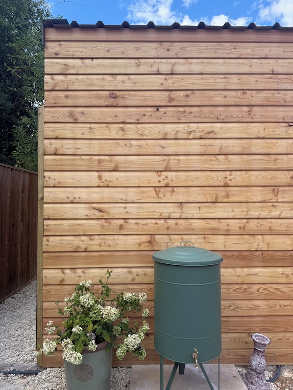 A wooden fence with a metal barrel and a potted plant with white flowers.