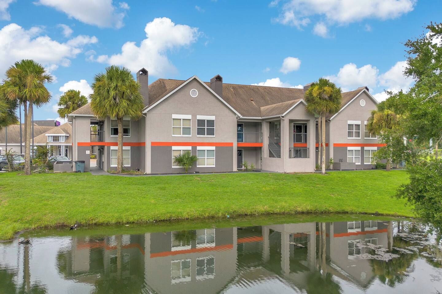 A multi-story residential building with a flat roof, a grassy lawn, and a small pond in the foreground.