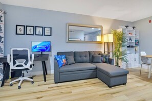 Un salon moderne avec un canapé d’angle gris, un bureau avec un ordinateur et un grand miroir.