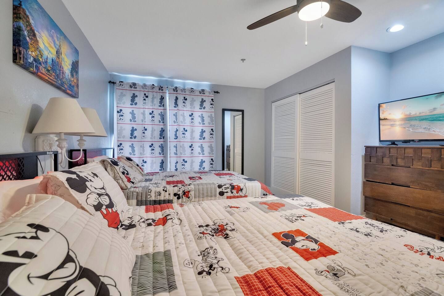 A bedroom with a large bed, a ceiling fan, a TV, and a painting on the wall.