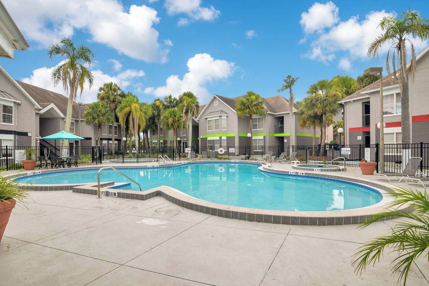 A swimming pool with a surrounding deck, palm trees, and a clear blue sky.