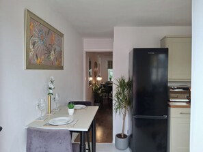 Eine kleine Küche mit einem schwarzen Kühlschrank, einem Esstisch mit Stühlen und einer Topfpflanze.