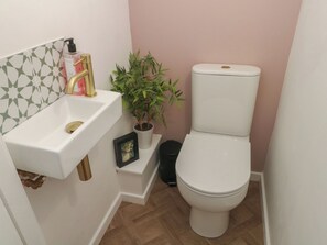 Ein kleines Badezimmer mit einem weißen Waschbecken, einer Toilette, einer Topfpflanze und einem gerahmten Bild auf dem Waschbecken.