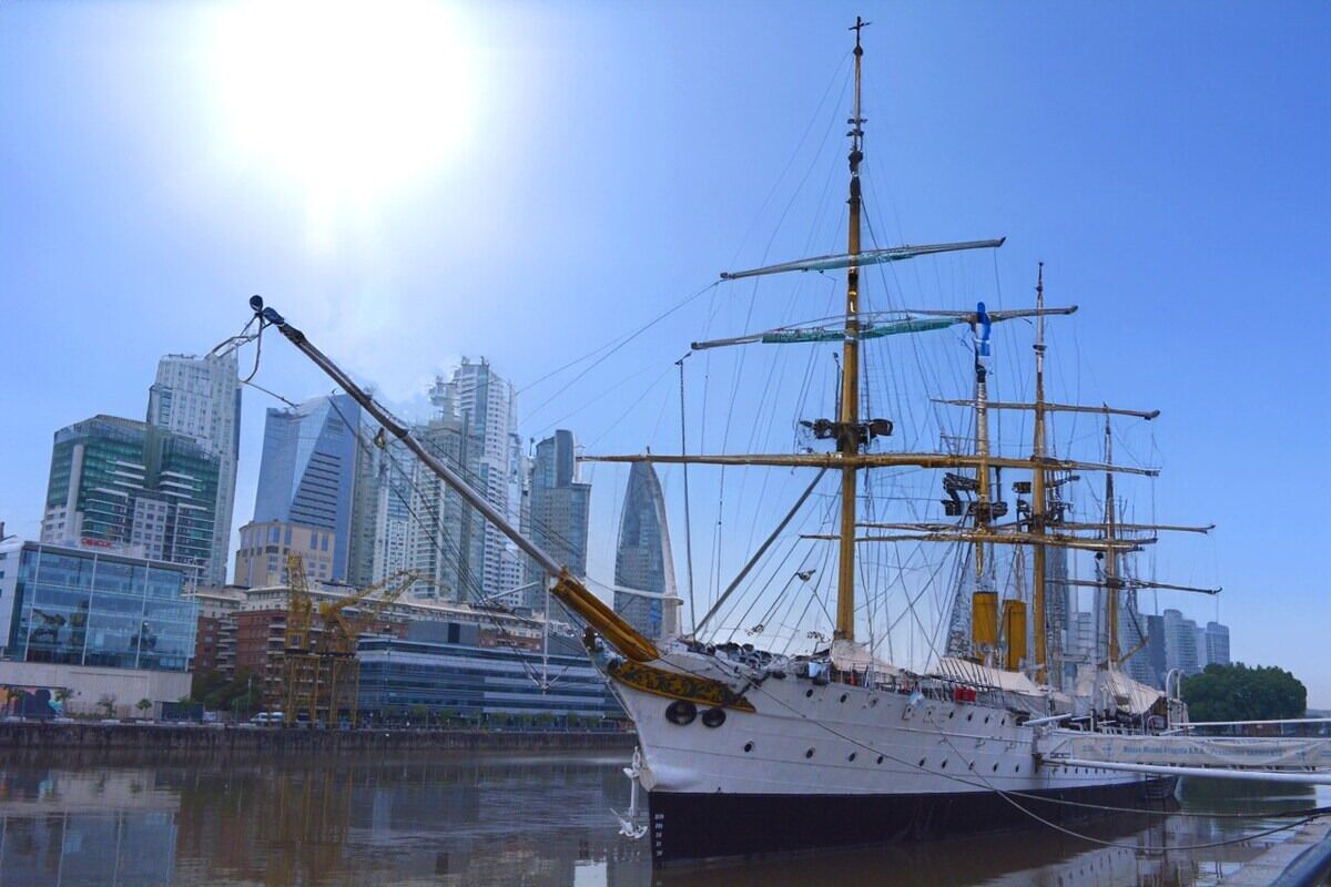 A tall ship docked in a harbor with a city skyline in the background.