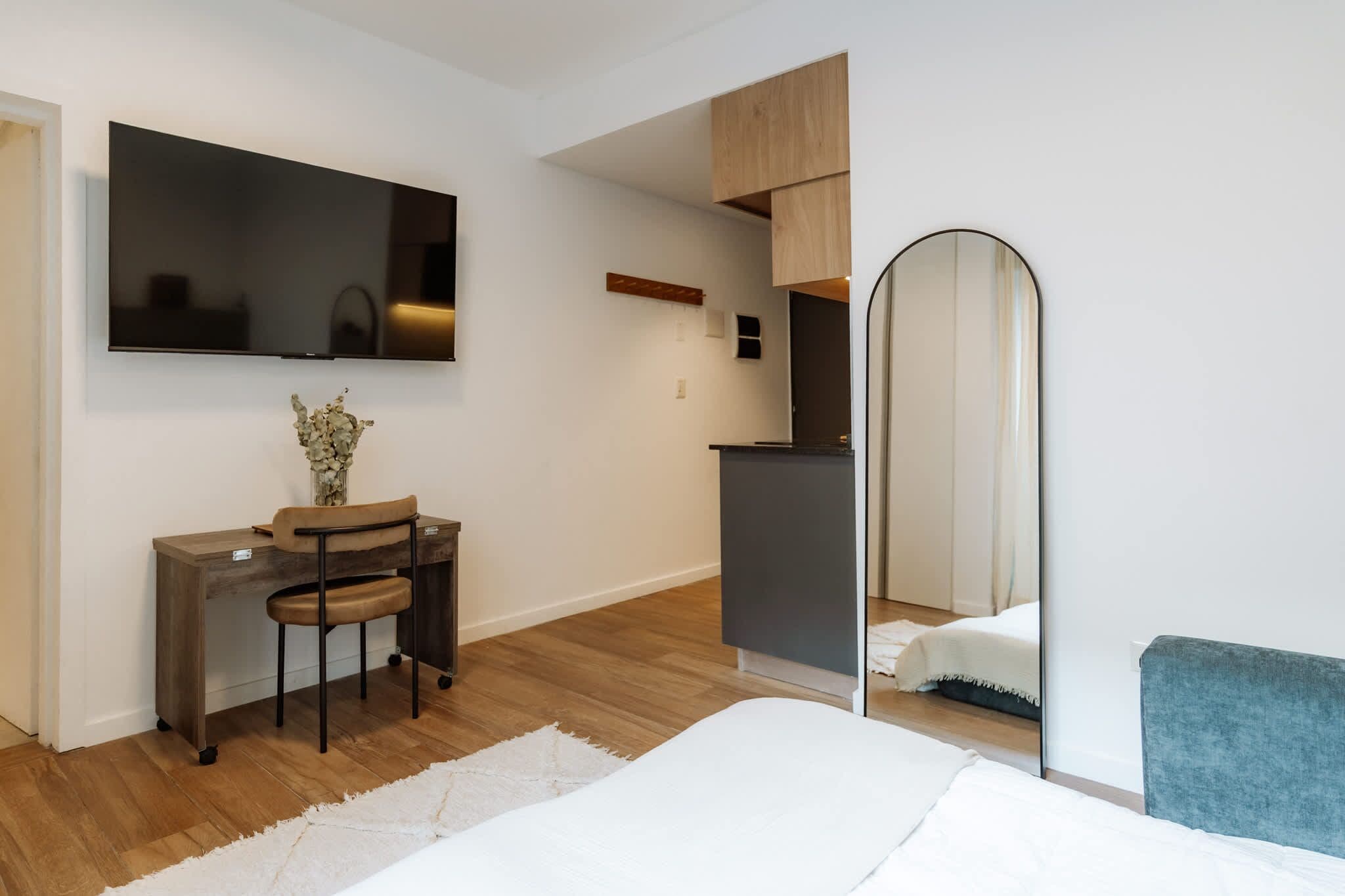 A modern bedroom with a bed, a desk with a chair, a television, a mirror, and a wardrobe.