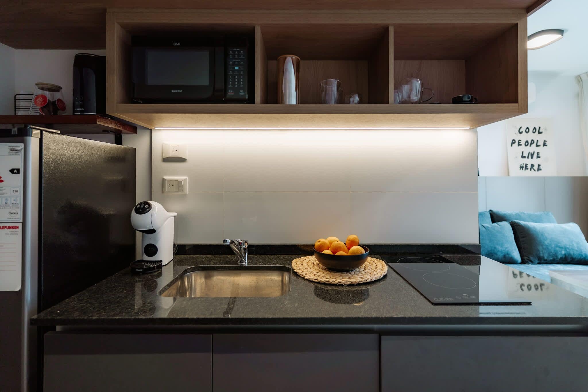 A modern kitchen with a built-in microwave, a coffee machine, a sink, and a bowl of oranges on the countertop.