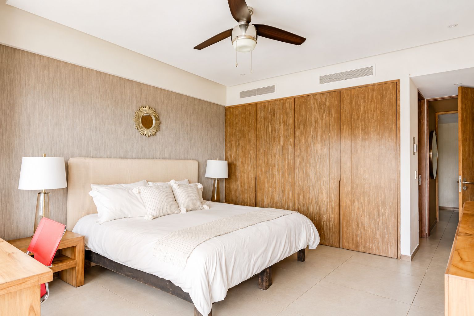 Un dormitorio con una cama, dos lámparas de noche, un ventilador de techo, un armario de madera y una pequeña mesa con una silla.