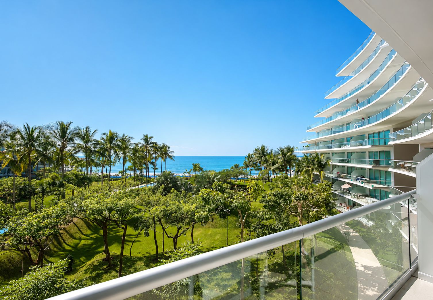 Un hotel moderno con balcón de vidrio con vistas a una playa y al océano.