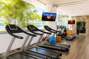 Uma academia com esteiras, bolas de exercício e uma tela de televisão.