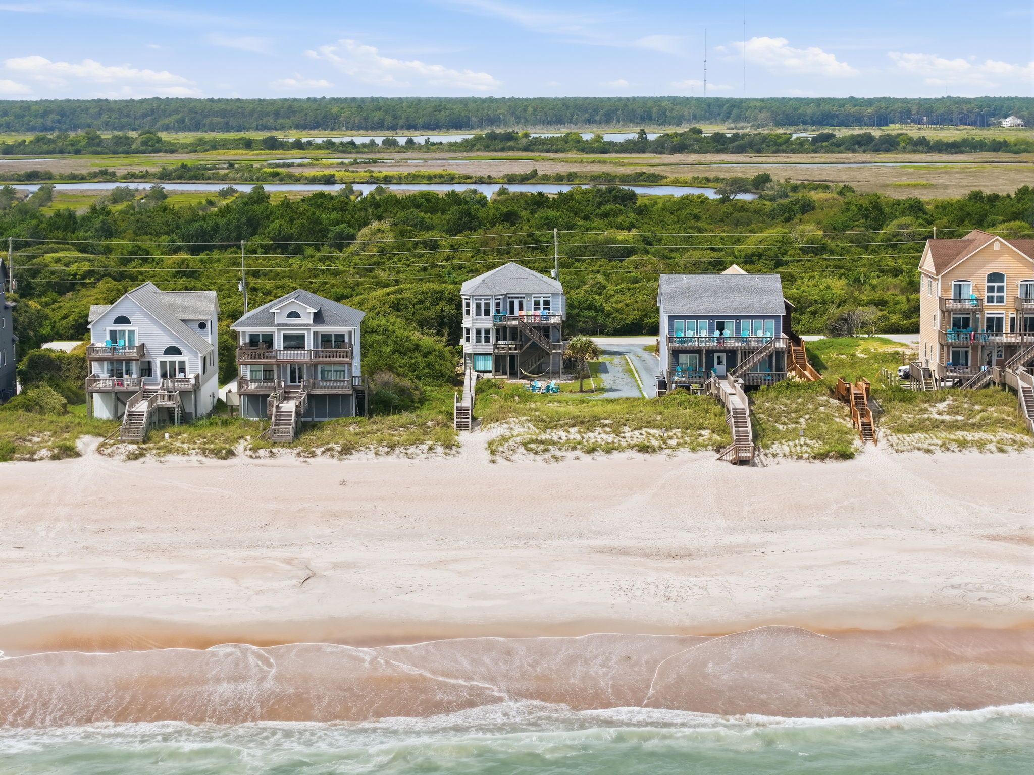 A beachfront property with multiple houses, each featuring a balcony and a view of the ocean.