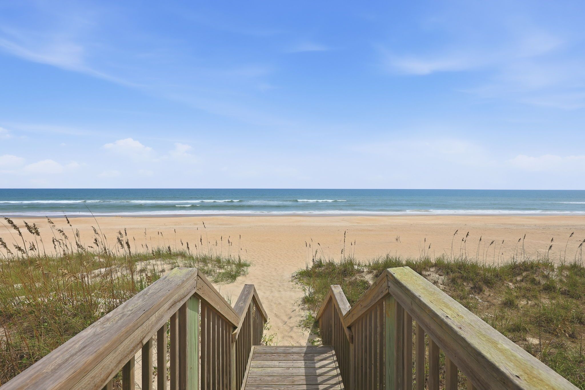 Ein hölzerner Steg führt zu einem Strand mit Blick auf den Ozean.