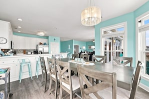 A modern kitchen with white cabinets, a dining area with wooden chairs, and a chandelier. - Almost Heaven | Beachside Living, Ocean Breezes (North Topsail Beach)