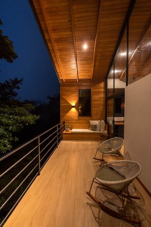 A wooden balcony with a seating area, two wicker chairs, and a table.