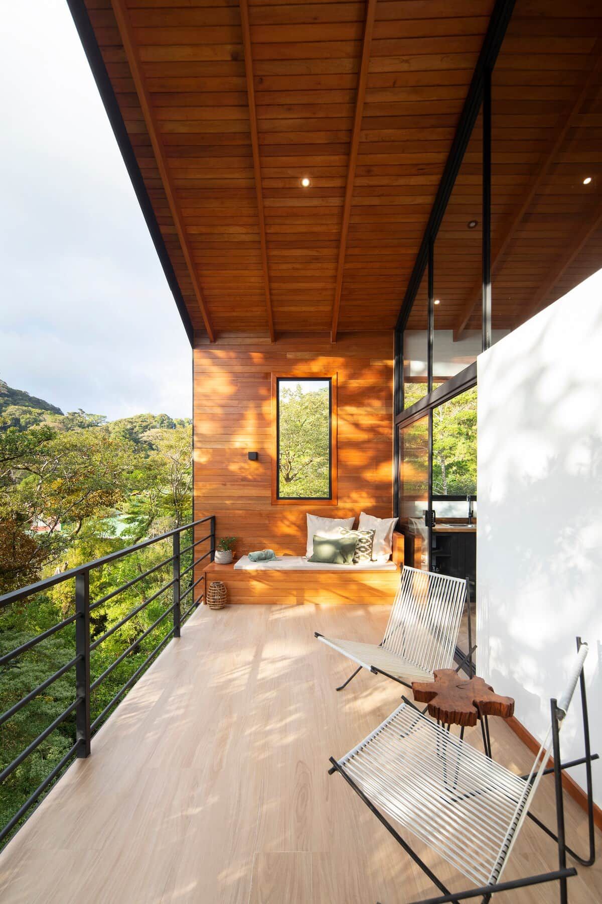 Un área de estar moderna al aire libre con techo de madera, vista del paisaje circundante y pared de vidrio.