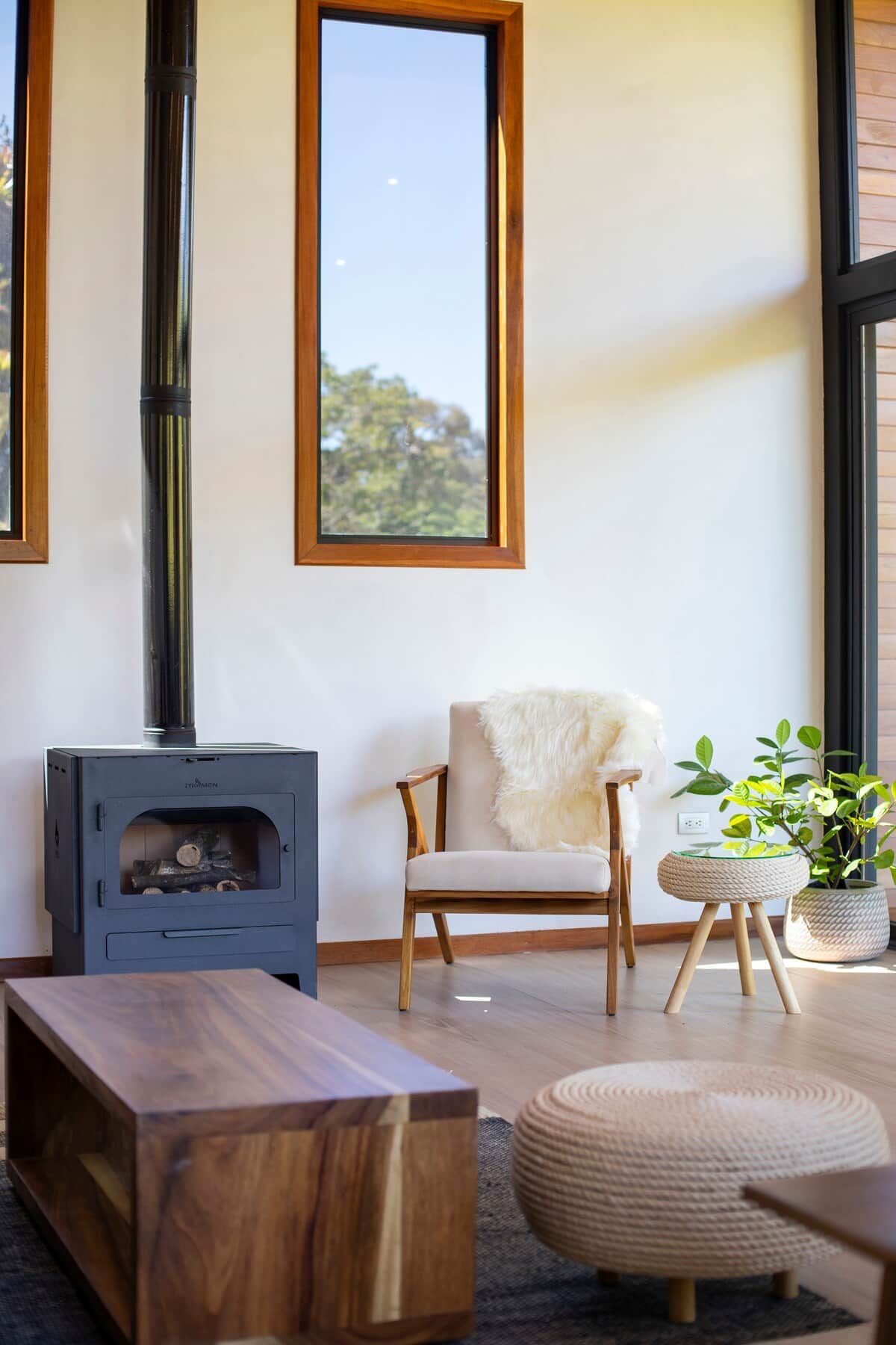 Una sala de estar moderna con una estufa de leña, un sillón cómodo, una mesa de centro de madera y un ventanal grande.