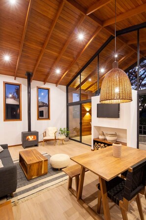 Ein modernes Wohnzimmer mit einem großen Holztisch, bequemen Sitzgelegenheiten, einem Kamin und großen Fenstern.
