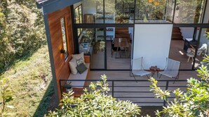 Een modern huis met een glazen gevel, een houten terras en een zitgedeelte buiten.