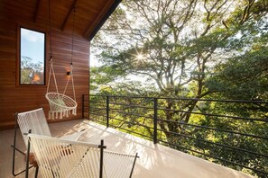 A balcony with a hammock chair, a white woven chair, and a view of trees. - Casa Jaguar (3) (Monteverde)