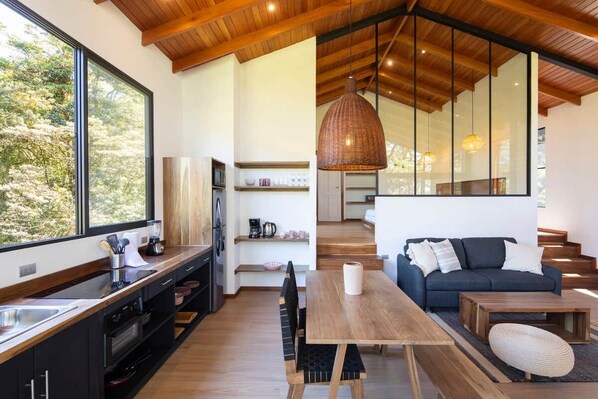 A modern kitchen with a large window, wooden ceiling, and a dining area with a table and sofa.