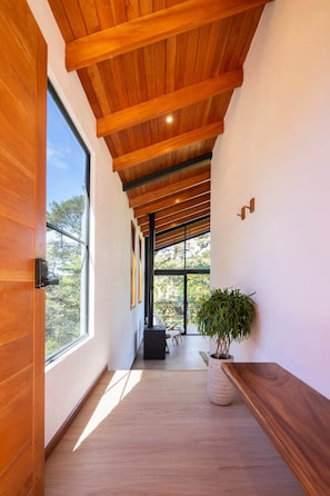 A hallway with wooden ceiling beams, large windows, and a potted plant. - Casa Jaguar (3) (Monteverde)