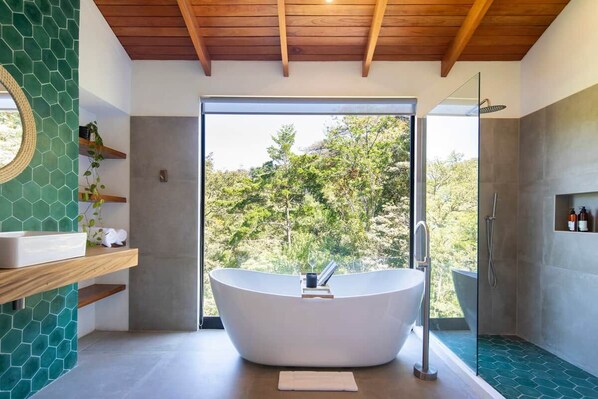 A modern bathroom with a freestanding bathtub, a glass shower enclosure, and a view of trees through a large window.