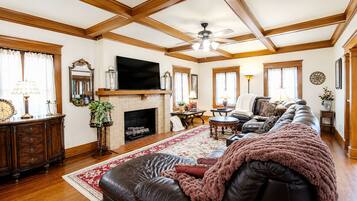 A spacious living room with a fireplace, leather sofa, and a television mounted on the wall.