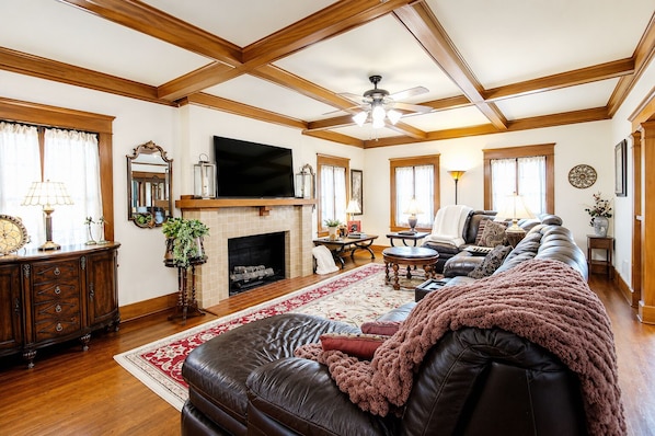 A spacious living room with a fireplace, leather sofa, and a television mounted on the wall.