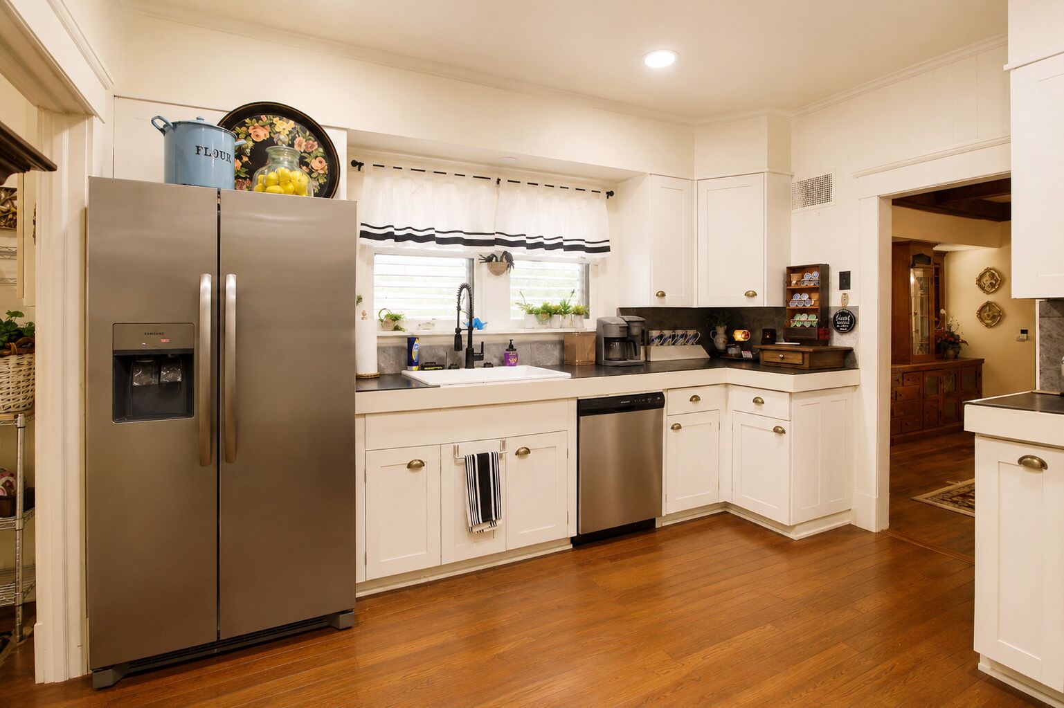 A kitchen with a stainless steel refrigerator, a dishwasher, and a sink with a striped window valance.