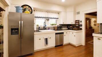 A kitchen with a stainless steel refrigerator, a dishwasher, and a sink with a striped window valance.
