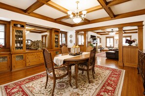 Ein Esszimmer mit Holztisch, Stühlen und einem roten Teppich mit Blumenmuster. Es gibt Holzschränke mit Glastüren und eine darüber hängende Chandelier.