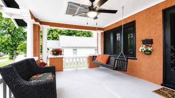 A covered porch with a swing, a wicker chair, a ceiling fan, and a door with a decorative handle.